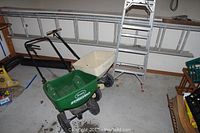 Photo showing both ladders and two lawn spreaders against a wall in garage.