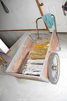 Wooden garden cart with metal frame, two large wheels visible, with several ropes inside.