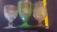 Three goblets shown side by side: clear glass goblet with leaf and grape pattern, green goblet with ribbed design, and another clear goblet with diamond pattern.