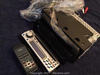 Car radio with silver faceplate and multiple control buttons, alongside a black remote control with labeled buttons.