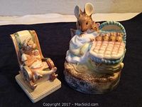 Photo showing two ceramic collectible figurines: a music box with a large mouse and smaller mice in a bed, and a smaller seated female figurine holding a baby.