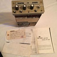 Front view of the Gralen Nav/Comm radio unit with frequency display, knobs, repair bill, and instruction manual visible.