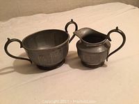 Hammered pewter sugar bowl and creamer set shown side by side on neutral background, clear view of design and size.