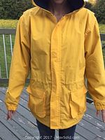 Photo showing the front view of a yellow fisherman's style jacket on a person, featuring a hood lined with black fleece, elastic cuffs, and front pockets with flaps.