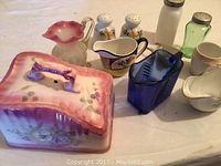 Photo of Nippon China salt and pepper, cobalt blue glass pitcher, milk glass, depression glass, and other assorted vintage decorative items on a table.