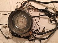 Round instrument console gauge with attached wiring harness showing aged condition, some wiring insulation tape, connectors visible.