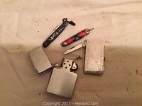 Photo shows three pen knives with differing handles and one Zippo lighter, displayed on fabric.