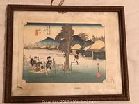 Framed Japanese woodblock print under glass in carved gilt wood frame, showing landscape scene with villagers and mountain.
