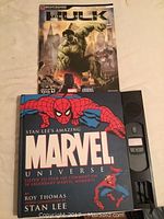 Photo showing the front covers of two Marvel books: Stan Lee's Amazing Marvel Universe hardcover featuring Spider-Man and the Incredible Hulk Sega Strategy Guide paperback with Hulk character image.