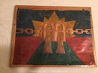 Frontal photo of a rectangular copper art piece mounted in a wooden frame. Features embossed AA logo with colored background and sunburst design.