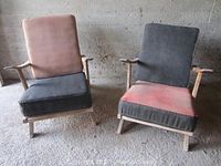 Front view of two mid-century armchairs with cushioned seats and backs, showing different cushion colors and fabric wear.