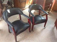 Pair of black office chairs with wooden frames and wheels on legs, showing front and side views.