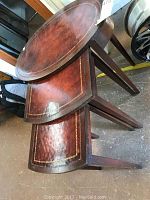 Three oval nesting tables stacked, showing the wood frames and leather tops with a gold embossed border pattern.
