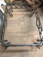 Full top-down view of large rectangular iron table base with decorative scrollwork on sides and corners, showing wear and rust.