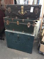Photo of three trunks stacked showing sizes, colors, and condition of exteriors including rust and dents