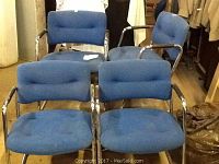 View of four blue upholstered chairs with silver metal frames and armrests.