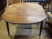 Front view of antique walnut drop leaf table showing oval top with drop leaves and turned legs.