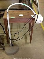 Wooden table with lamp on top, lamp has flexible arm and round head, showing signs of wear and age.