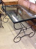 View of the full table showing black iron scrolling frame and glass top.