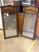 Pair of two rectangular matching mirrors with plastic simulated wood frames, decorative detailing on top panel, standing upright.
