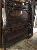 Full view of carved wooden headboard and footboard leaning against a wall, showing dark wood and carved panel details.