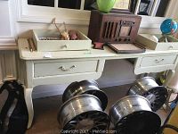 Front view of the wooden desk showing the top with items placed on it and the lower drawers with metal handles.
