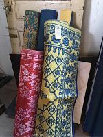 Five rolled plastic outdoor rugs in assorted colors and patterns leaning against a door.