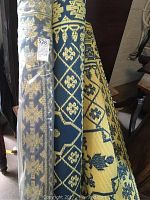 Five rolled and partially unrolled plastic outdoor rugs in blue-beige floral patterns and multicolor stripes, some wrapped.