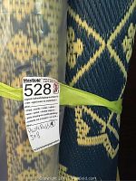 Four rolled plastic rugs stacked with yellow strap and MaxSold tag indicating quantity and size 5x8