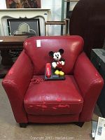 Full view of red armchair with visible wear and vintage Mickey Mouse phone on seat.
