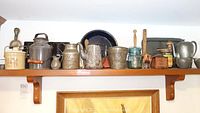 Shelf displaying a group of vintage mixed metal kitchen items including the milk can, cheese crock, canisters, and jars.