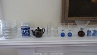 Wide side view of items on white shelf showing glass bowls, Delft vase, small teapot, clear glasses with blue ball stems, martini glass, and small blue and white items