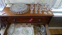 Wide view of the collection including wine glasses, trays, and smaller serving pieces on a wooden sideboard.