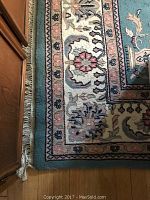 Close-up showing rug border with floral patterns and fringe on wooden floor.