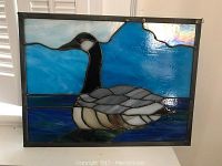 Frontal view of stained glass art featuring a goose on water with blue sky, showing color details and framing.