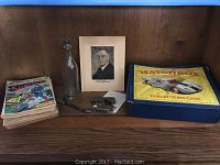 Overview photo showing stacked vintage comic books including Superman comics, a vintage Matchbox collectors case, glass bottle, small metal toys and tools, and a framed photo.