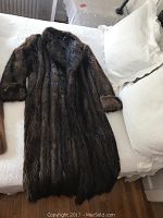 Full vintage beaver fur coat laid out flat on white bedding to show length and condition