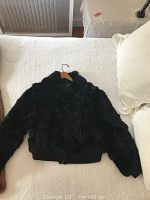 Full view of the black rabbit fur jacket laid flat showing shape, fur texture, and ribbed hem and cuffs.