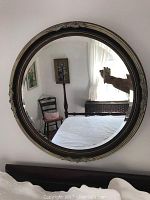 Front view of the carved wood circular mirror hung on a wall, showing a bedroom reflected in the glass.