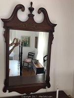 Front view of large carved wood mirror showing detailed top scrollwork, central finial, and floral carvings, with some minor wear visible on frame edges