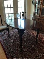 Solid carved wood oval dining room table with polished surface, carved legs with claw feet, viewed from side.
