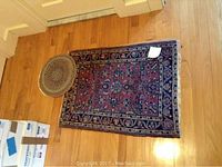 Large rectangular oriental style area rug with floral design and a smaller round braided rug on hardwood floor.