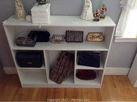 Full frontal view of white wood bookcase with six shelves, holding small bags and figurines.