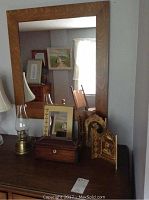 Wood-framed mirror on wooden dresser with an oil lamp, wooden jewelry box with drawer, and religious triptych icon on the dresser surface.