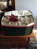 Photo showing the padded case containing 12 red colored wine goblets individually wrapped in protective paper with one glass placed on top of paper inside the case.