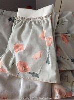 Close-up of floral patterned fabric on bed linens and pillow shams showing peach flowers and greenery on light fabric.
