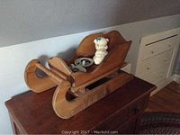 Photo of vintage wooden sled with a white ceramic piggy bank with a blue bow sitting inside the sled.
