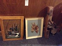 Three rustic vintage decor items side by side against wooden paneling, including two framed artworks and one tall wooden sculptural hanging piece.