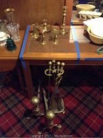 Metal fireplace tool set displayed on floor with stand, showing age-related rust and wear.