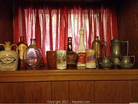 Wide view showing all items including vintage jugs, pewter teapot and teacups, decorative cups and multiple bottles in various materials on a wooden shelf.